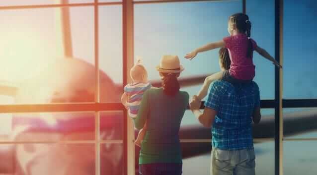 father, mother, flying daughter and baby at an airport looking at a plane with sun in the background